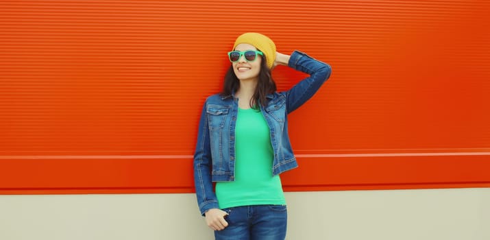 Happy smiling young woman in summer, wearing a sunglasses, bright hat, denim jacket, posing against colorful wall on city street