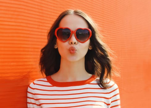 Portrait of beautiful cute brunette young woman blowing kiss with red heart shaped sunglasses in the city