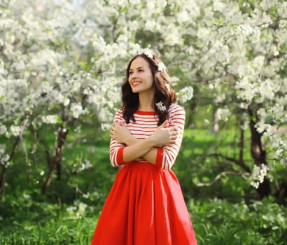 Portrait of lovely happy smiling young woman in spring blooming garden with white flowers on the trees in park