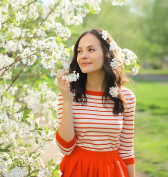 Portrait of lovely happy smiling young woman in spring blooming garden with white flowers on the trees in park