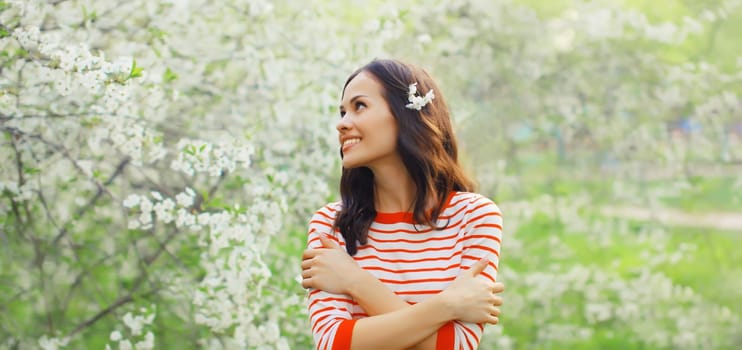 Portrait of lovely happy smiling young woman in spring blooming garden with white flowers on the trees in park