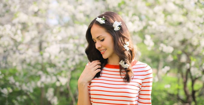 Portrait of lovely happy smiling young woman in spring blooming garden with white flowers on the trees in park