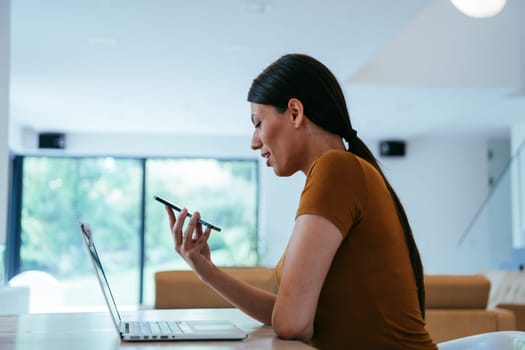 A woman sitting in the living room using a laptop and a smartphone look at camtalk by video call with business friends and relatives, head shot. Job interview answering questions
