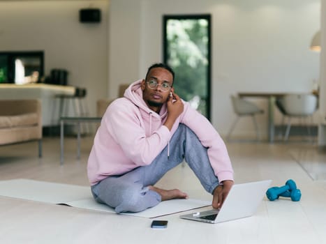 African American man in glasses sitting at a table in a modern living room, using a laptop for business video chat, conversation with friends and entertainment