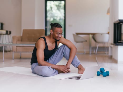 Training At Home. Sporty man doing the training while watching an online tutorial on a laptop, exercising in the living room, free space