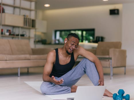 Training At Home. Sporty man doing the training while watching an online tutorial on a laptop, exercising in the living room, free space