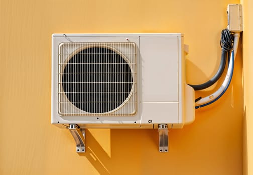 Outdoor air conditioning system mounted on a yellow wall. Concept of energy efficiency, modern climate control, and summer cooling solution. Clean and minimal design.