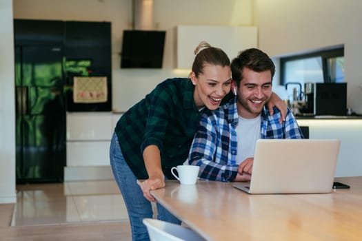 A young married couple is talking to parents, family and friends on a video call via a laptop while sitting in the living room of their modern house