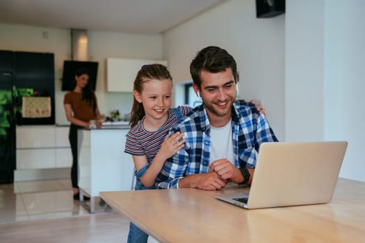 Work from home. Daughter interrupting her father while he is having a business online conversation on his laptop while sitting in the modern living room