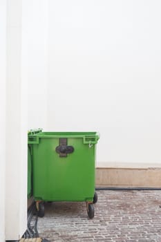 A green trash bin sits quietly in the corner of a minimalist space.