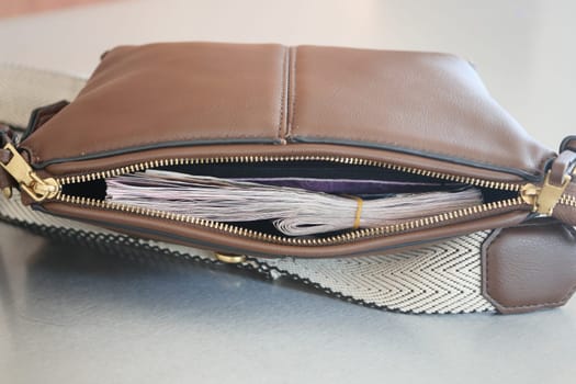A brown bag sits on a table with cash partially visible from the zipper.