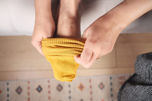 A person puts on a soft yellow sock while seated on a comfortable surface.