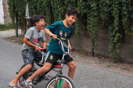 Two happy friends of teenage boy ride a bike during the summer holidays. Shymkent, Kazakhstan - July 12, 2024