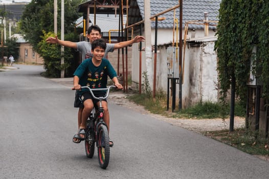Two happy friends of teenage boy ride a bike during summer holidays in Kazakhstan. Shymkent, Kazakhstan - July 12, 2024