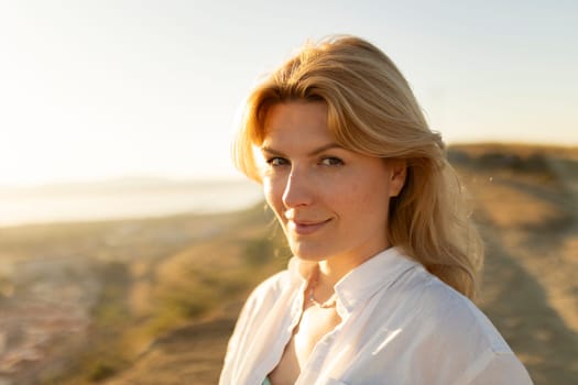 Portrait of a smiling blonde woman enjoying the golden hour sunlight on a hill