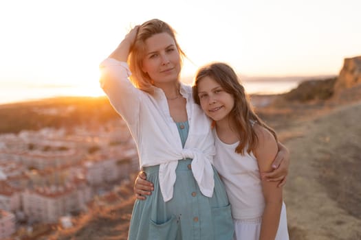 Mother and daughter hugging on a hill overlooking a cityscape during a beautiful sunset