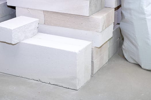 A neat pile of white bricks is positioned next to a large white bag, showcasing their contrasting textures and colors against each other