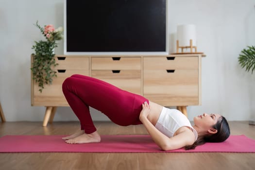 This image shows a woman doing the bridge pose, which strengthens core muscles and enhances flexibility in a comfortable home setting.