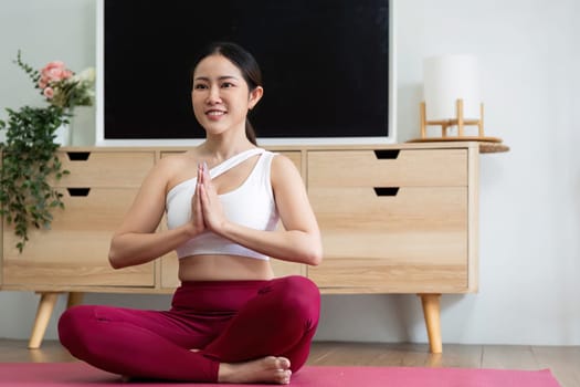 In a serene indoor setting, a woman sits with her hands in a prayer pose, embodying tranquility during her yoga practice. The image highlights the importance of mindfulness and physical wellness.