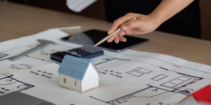 A close-up of a hand discussing a small house model on top of blueprints. This exchange highlights the essential planning that goes into construction and architecture.