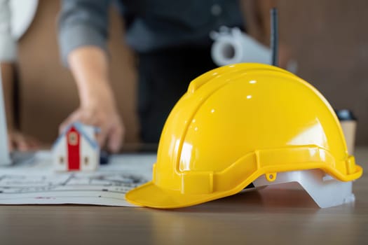 A construction engineer's hard hat is placed beside detailed blueprints. It signifies the importance of safety and planning in construction projects, embodying the collaborative nature of engineering.