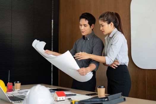 Two engineers share insights over project plans, reflecting collaboration and innovation in their workspace. Their engagement demonstrates teamwork in architectural design.