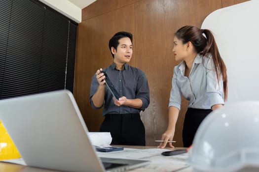 Two engineers engage in a brainstorming session, exchanging ideas and discussing project elements around a conference table filled with plans and models.