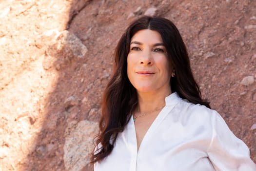 Portrait Of Smiling Lebanese Woman In Her 50 in White Shirt Outside, Red Rocks On Background. Sunny Day. Beautiful Confident Fashionable Female Outdoor, Middle Eastern Attractive Person. Horizontal.