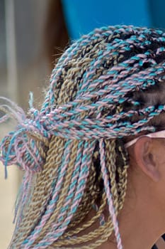 A close-up of colorful braids interwoven with shades of blonde, pink, and blue. The intricate twists and neat styling create a striking visual effect, showcasing creativity and attention to detail.