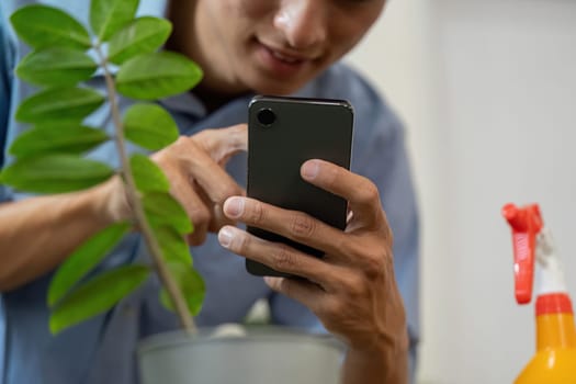 A close-up shot of someone engaged in smartphone use while taking care of a potted plant, showing a modern approach to gardening.