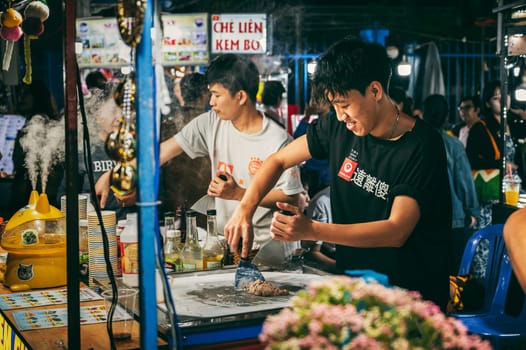 Vietnamese young male cook make ice cream at a asian Night market of street food stand in Da Nang in Asia. Da Nang, Vietnam - November 30, 2024