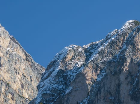 Close up view of rugged, steep mountain peaks with textured rocky surfaces and patches of snow, set against a clear blue sky in the Dolomites.