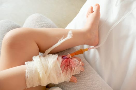 Close up of baby's hand inpatient with intravenous infusion set to drop the normal saline and injection to treat in the hospital, concept of kid illness and hospital care.