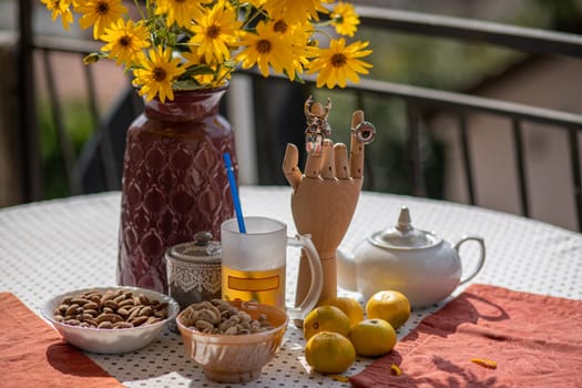 A vibrant table setting displays a vase filled with yellow flowers, various bowls of nuts, a teapot, and a distinctive wooden hand statue. The warm sunlight enhances the inviting atmosphere.