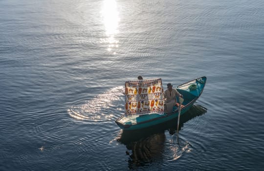 Esna, Egypt - 3 November 2024: Nile River on a sunny day featuring a vendor in a small rowboat selling textiles to a cruise ship.