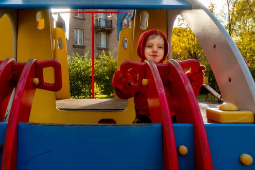 Child with red raincoat of firefighter clings to a rope in a playground during rain. High quality photo