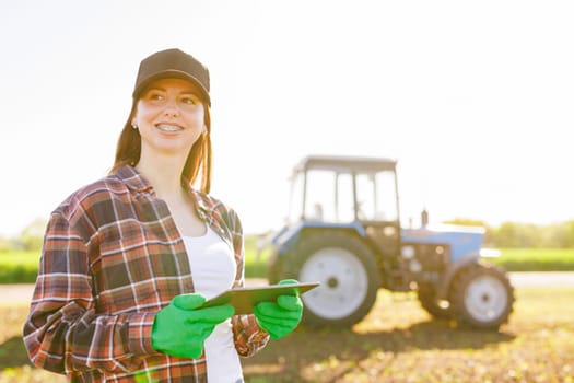 a girl agronomist with a tablet manages agribusiness against the background of a tractor, modern agribusiness