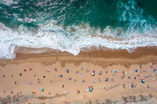 Overhead drone shot of tourists and parasols on sandy beach. A top-down view of people enjoying summer vacations by the sea on a sunny day