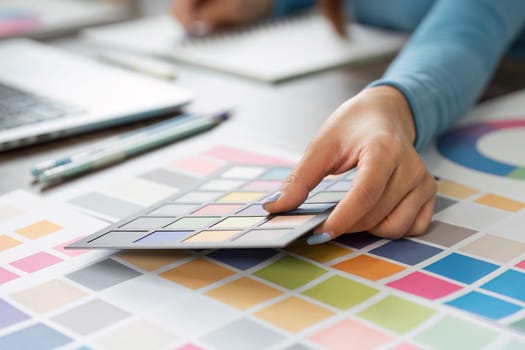 In a dynamic workspace, a designer is engaged in selecting colors from a physical palette while using a laptop.