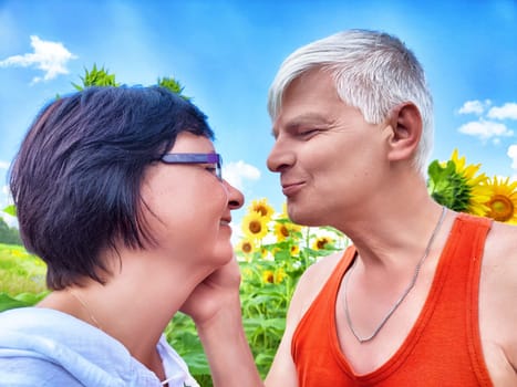 A middle-aged couple enjoys a tender moment in a vibrant sunflower field. They share smiles and affectionate gestures while surrounded by nature's beauty on a sunny day.