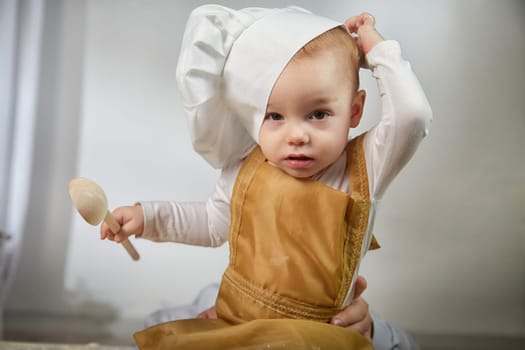 A curious boy wearing a chef's hat gazes thoughtfully while her photo is taken in a warm and inviting studio space.