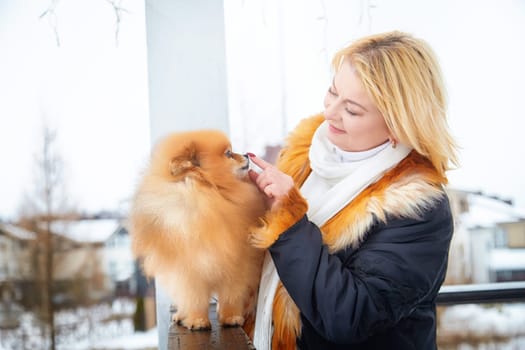 A middle-aged woman lovingly interacts with her fluffy pomeranian dog during a cold winter day.