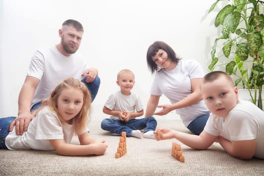 A family happily builds wooden block structures together on a soft rug in their living room.