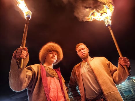 Actors in traditional ethnic costumes perform a captivating fire show under the cold winter night sky, embodying brave warriors from history.