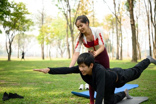 Smiling young woman assisting partner with stretching in outdoor yoga session.