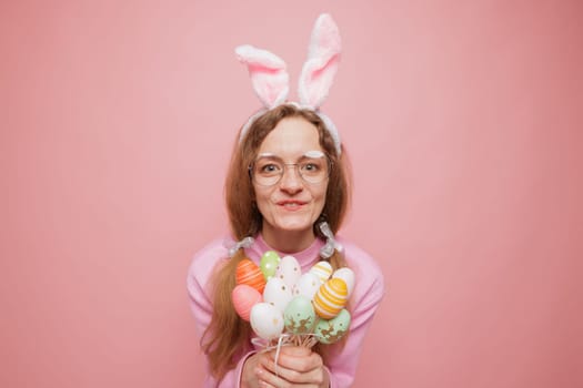 Happy woman in bunny ears holding a bouquet of colorful Easter eggs, smiling playfully. Festive spring mood, holiday joy, and seasonal celebration