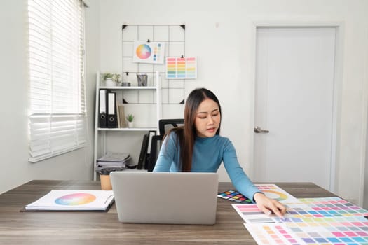 The designer engages with various color selections, creating a harmonious balance between digital tasks and hands-on color exploration in a professional setting.