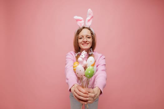 Happy woman in bunny ears holding a bouquet of colorful Easter eggs, smiling playfully. Festive spring mood, holiday joy, and seasonal celebration