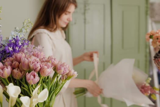 Female florist creating a delicate bouquet with fresh flowers in a floral workshop, surrounded by colorful blooms in glass vases. flower shop