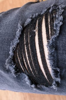 A detailed closeup view highlighting a hole found in a pair of ripped jeans, showcasing the texture and wear of the fabric